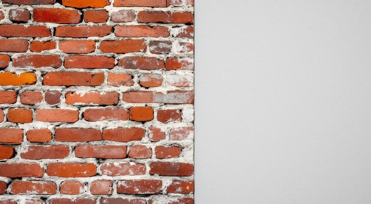 Mur de brique dont une moitié est laissée brute et l'autre recouverte d'une peinture gris clair opaque